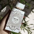 Zimaya Musk Is Great by Zimaya 100ml EDP Unisex — A white perfume bottle with a geometric pattern and gold accents, held in a hand with green bamboo leaves in the background.