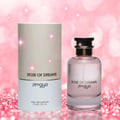 Zimaya Rose of Dreams — A clear glass perfume bottle with pink liquid and a black and gold cap, next to its cylindrical beige and white box, set against a sparkling pink bokeh background.