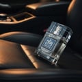 Zimaya Mazaaj Infused by Zimaya 100ml EDP Men — Clear glass perfume bottle with a blue label, resting on a black leather car seat with warm lighting.