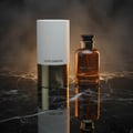 Zimaya Night Shadow by Zimaya 100ml EDP Unisex — A white and gold cylindrical box stands next to a brown glass perfume bottle with a black cap, both on a reflective black marble surface with a smoky background.