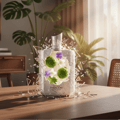 Zimaya Phantom Paragon by Zimaya EDP 100ml Man — A white perfume bottle shattered with green kaffir limes and purple flowers inside, set on a wooden table with plants in the background.