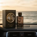 Zimaya Reverie Aqua by Zimaya 100ml EDP Men — Black textured box and glass bottle with gold sun and wave design, placed on car dashboard with ocean sunset background