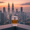 Zimaya Sharaf Blend by Zimaya 100ml Extrait de Parfum — A clear glass perfume bottle with amber liquid sits on a dark surface against a hazy city skyline at sunset, featuring the Petronas Twin Towers.