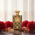 Zimaya Siada Nova by Zimaya 100 ml EDP — Gold-capped dark glass bottle with ornate gold pattern, surrounded by red roses and amber-colored resin pieces on a dark reflective surface.