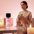 Zimaya Yaa Umree by Zimaya EDP 100 ml Women — Pink perfume bottle with Arabic calligraphy and 'Yaa Umree' text, placed on a table with lit candles and a woman in a pink robe holding a teacup in the background.