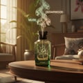 Zimaya Oscar by Zimaya 100ml EDP Men — Green glass perfume bottle with black cap, emitting wisps of smoke labeled 'MUSK' and 'CEDARWOOD', set on a wooden table in a living room.