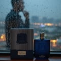 Zimaya Royal Paragon EDP 100ml Man — A blue glass perfume bottle and its dark striped box sit on a wooden surface, with a blurred man looking out a rain-streaked window in the background.