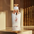 Zimaya Taraf White by Zimaya 100ml EDP Women — White perfume bottle with rose gold accents and Arabic calligraphy logo, set against a blurred golden background with vertical elements.