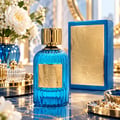 Paris Corner Qissa Blue by Paris Corner 100ml EDP Unisex — Botol minyak wangi kaca biru berjalur dengan penutup emas dan label timbul emas, bersebelahan kotak biru dan emasnya, dengan bunga putih dan pasu biru di latar belakang.