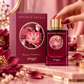 Zimaya Reverie Petals by Zimaya 100ml EDP Women — A woman's hand with dark red nails reaches for the gold cap of a deep red perfume bottle, next to its matching box, surrounded by pink and red floral petals and delicate white flowers on a marble surface.