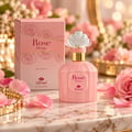 TADangel Rose Divine by TADangel 100ml EDP Women — Pink perfume bottle with a decorative white and gold cap, next to its matching pink box adorned with rose illustrations. Surrounded by pink rose petals and flowers on a marble surface.