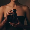 Bujairami Sacred Skin Bujairami 100ml Extrait Unisex — Woman's hands with intricate henna designs holding a dark red perfume bottle with a black cap.