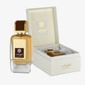 Ard Al Zaafaran Shahrazad Eau De Parfum 100ml — Botol wangian emas berkilat dengan penutup coklat dan emas, diletakkan di sebelah kotak hadiah putih terbuka yang memaparkan botol kecil dan reka bentuk daun emas.