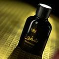 Gulf Orchid Shumookh Parfum 100ml by Gulf Orchid — A black perfume bottle with a gold crown logo and Arabic script, tilted on a textured gold surface. | Gulf Orchid Shumookh Parfum 100ml by Gulf Orchid — Botol minyak wangi hitam dengan logo mahkota emas dan tulisan Arab, condong di atas permukaan emas bertekstur.