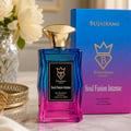 Bujairami Soul Fusion Intense — A gradient blue to pink glass perfume bottle with a gold cap, next to its matching box. White flowers in a vase and a gold tray are visible.