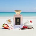 Bujairami Sugar Rush by Bujairami Eau de Parfum — Perfume bottle on a sandy beach with a blurred ocean background, surrounded by strawberries, marshmallows, raspberries, vanilla beans, and whipped cream.
