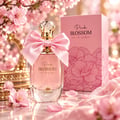 TADangel Pink Blossom 100ml EDP Women — Pink perfume bottle with a large satin bow and crystal cap, next to its pink box adorned with floral patterns, surrounded by pink cherry blossoms and petals.