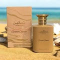 Paris Corner Taskeen Caramel Cascade 100ml — A perfume bottle and its box sit on a sandy beach with the ocean in the background. | Paris Corner Taskeen Caramel Cascade 100ml — Botol minyak wangi dan kotaknya diletakkan di pantai berpasir dengan lautan di latar belakang.