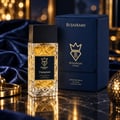 Bujairami Tempted 100ml Extrait Perfume Unisex — A square, faceted glass perfume bottle with golden liquid and a black cap, placed on a reflective dark surface next to its navy blue presentation box. The background features blurred golden lights and dark blue velvet fabric.