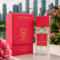 Bujairami Too Damn Clean 100ml Extrait — Red presentation box and clear glass perfume bottle with red cap, set against a blurred city skyline and pink flowers.