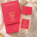Bujairami Too Damn Clean — A clear glass perfume bottle with a textured red cap and a pink label featuring a gold crown and 'B' logo, placed next to its matching pink presentation box with gold lettering and logo.
