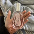 Ard Al Zaafaran Yara Eau De Parfum 50ml — A hand holds a clear, pink-tinted perfume bottle with a silver cap and a pink label featuring Arabic script and the word YARA. The hand has henna designs on the palm. | Ard Al Zaafaran Yara Eau De Parfum 50ml — Tangan memegang botol minyak wangi jernih berwarna jambu dengan