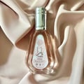Ard Al Zaafaran Yara Eau De Parfum 50ml — A clear glass perfume bottle with a pink label and silver cap, resting on draped pink satin fabric. | Ard Al Zaafaran Yara Eau De Parfum 50ml — Botol minyak wangi kaca jernih dengan label merah jambu dan penutup perak, diletakkan di atas fabrik satin merah jambu yang dilipat.