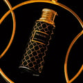 Maison Asrar Treasure by Maison Asrar 100ml EDP Unisex — Botol hitam corak geometri emas dan penutup emas, dipamerkan dalam bingkai bulat emas berlatar belakang hitam.