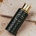 Treasure by Maison Asrar 100ml EDP Unisex — Botol hitam corak geometri emas dan penutup emas, diletakkan atas batu bertekstur.