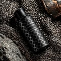 Maison Asrar Vanguard by Maison Asrar 100ml EDP Unisex — Botol hitam corak geometri perak, atas lapisan rantai besi dan batu, dengan cebisan perisai di latar belakang.
